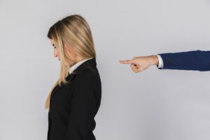 businessman-s-hand-blaming-young-businesswoman-against-grey-backdrop-1200x800